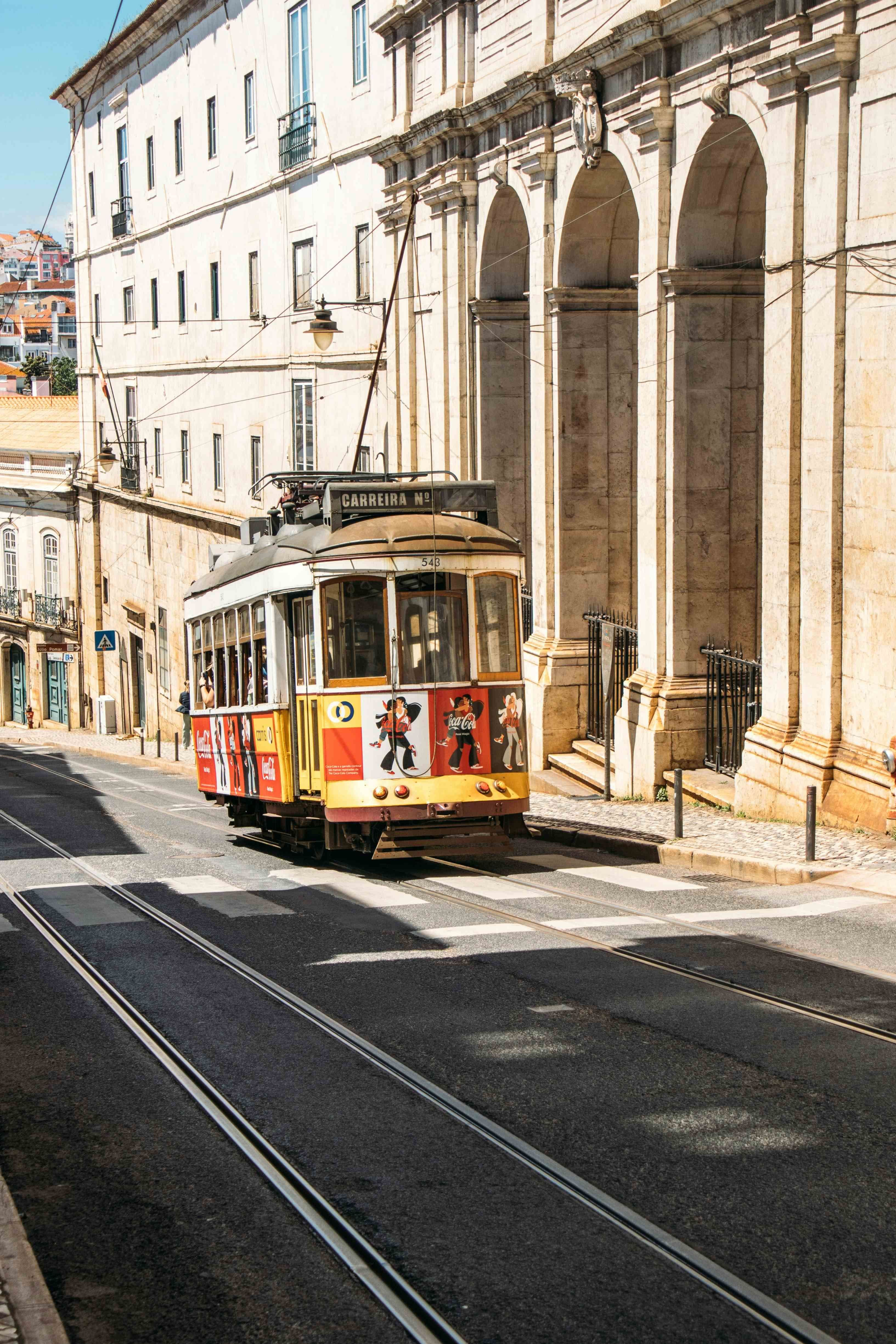 Yellow tram on a Lisbon street, with historic buildings in the background.